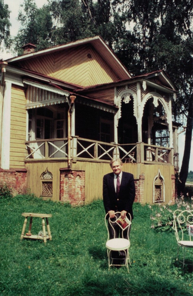 Alexander Kugushev in front of a wooden dacha in Russia