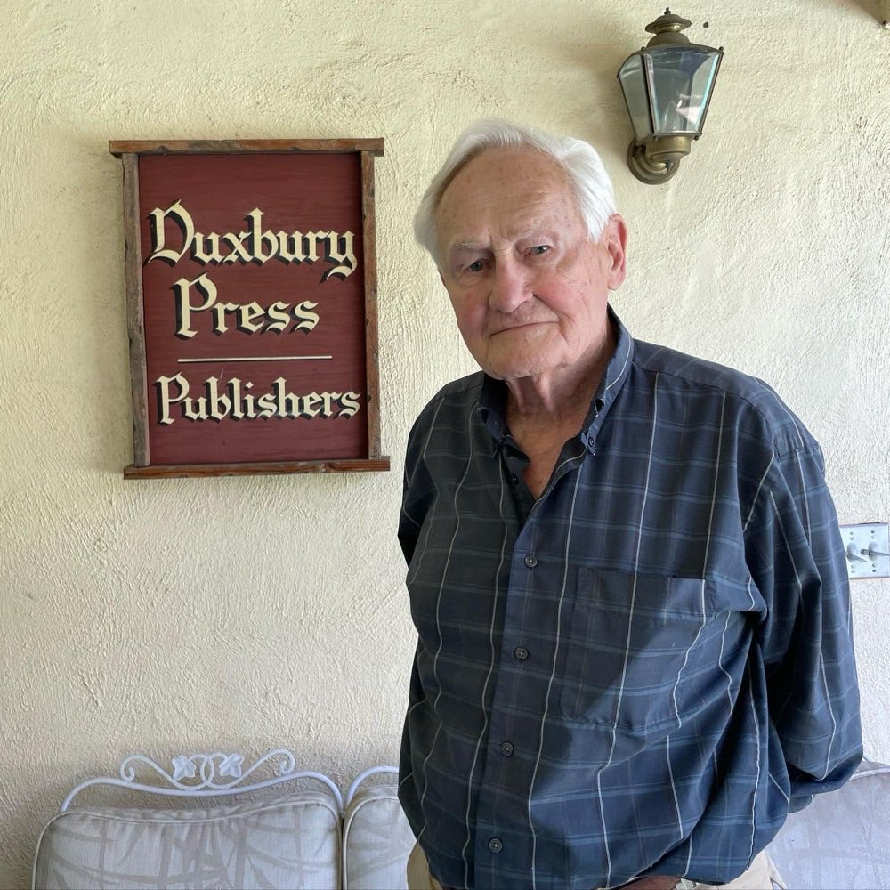 Alexander Kugushev standing by a Duxbury Press Publishers sign